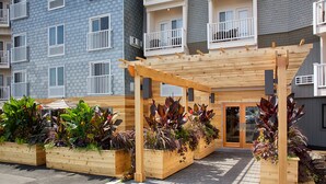 A covered outdoor area with wooden planters filled with various plants, a wooden pergola, and a building with balconies in the background. - Rockland Harbor Hotel (Rockland)