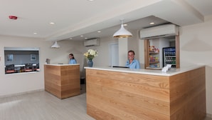 A reception area with wooden reception desks, a refrigerator stocked with beverages, and a window with a view of the outside. - Rockland Harbor Hotel (Rockland)