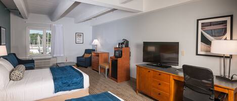 Ett hotellrum med två sängar, ett skrivbord, en stol, en tv och ett fönster med utsikt över båtar.