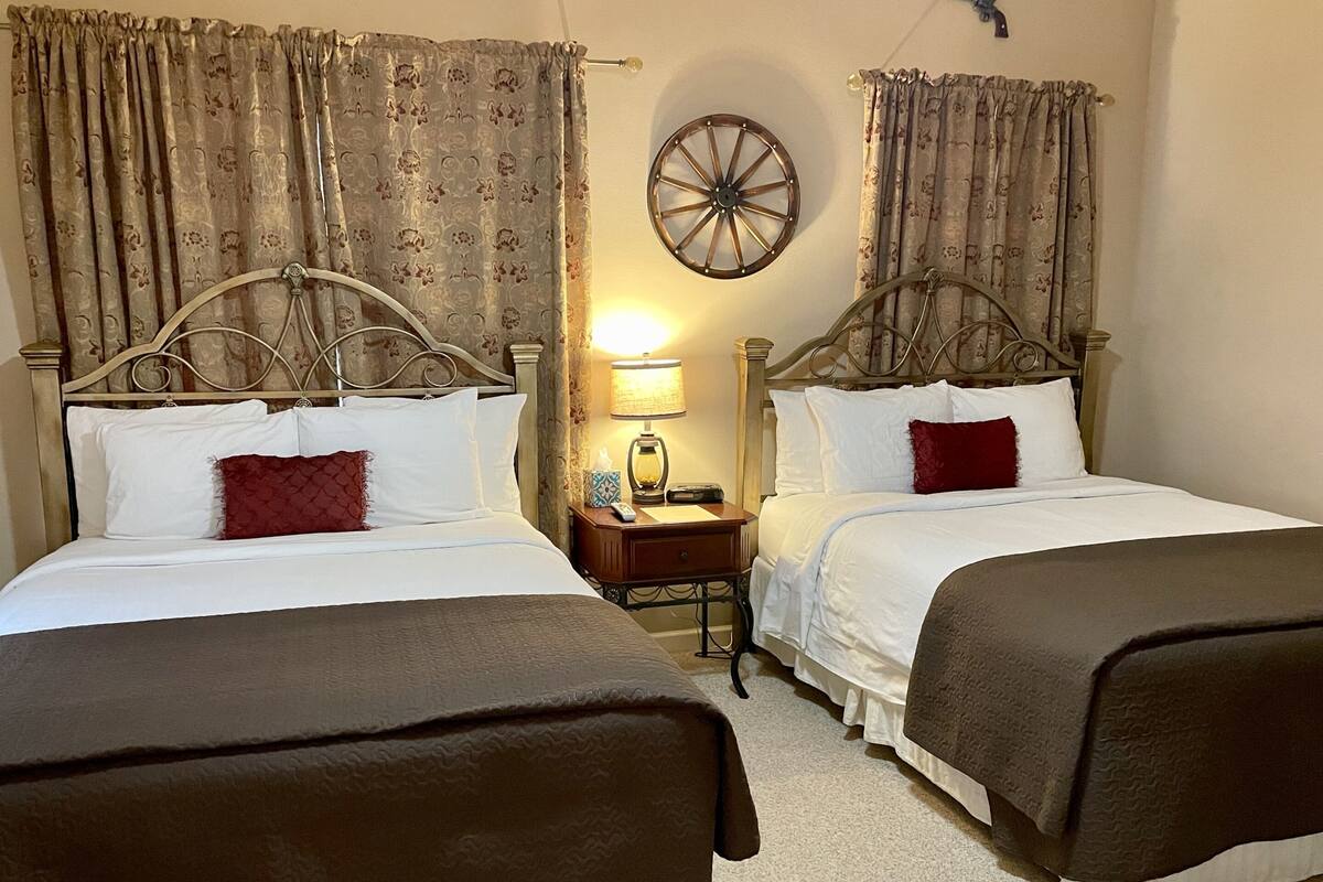 Habitació d'hotel amb dos llits individuals, cadascun amb un capçal, una tauleta de nit amb una làmpada i una roda decorativa penjada a la paret.