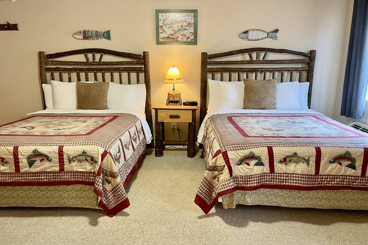 Una habitació amb dos llits de fusta, cadascun amb un llençol estampat amb motius de peixos. Hi ha una tauleta de nit amb una làmpada entre els llits.
