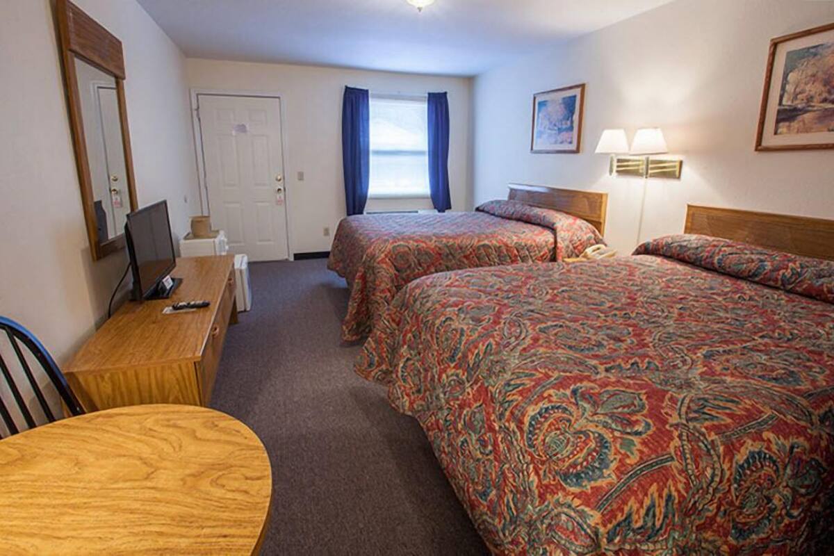 Une chambre d’hôtel avec deux lits, un bureau avec un ordinateur, une chaise, une lampe et une fenêtre avec des rideaux.