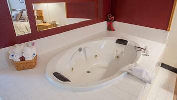 A bathroom with a large white bathtub, a mirror, a basket of towels, and a vase with flowers.