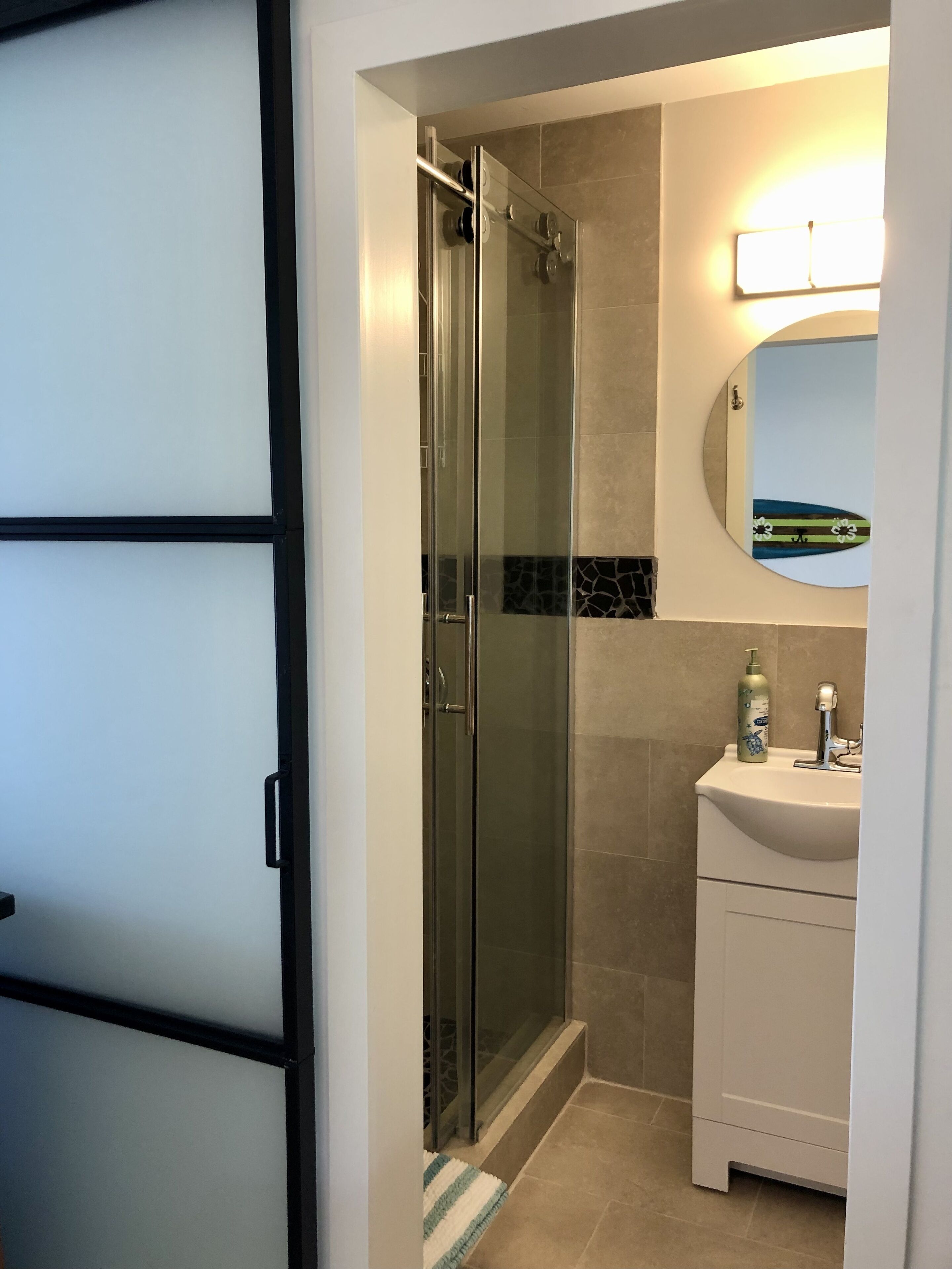 A modern bathroom with a glass-enclosed shower, a white sink with a mirror above it, and a tiled floor.
