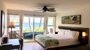 Habitación de hotel con cama, escritorio, silla, ventilador y vista al océano.