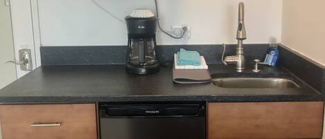 A compact kitchen with a dishwasher, a coffee maker, a microwave, and a sink.