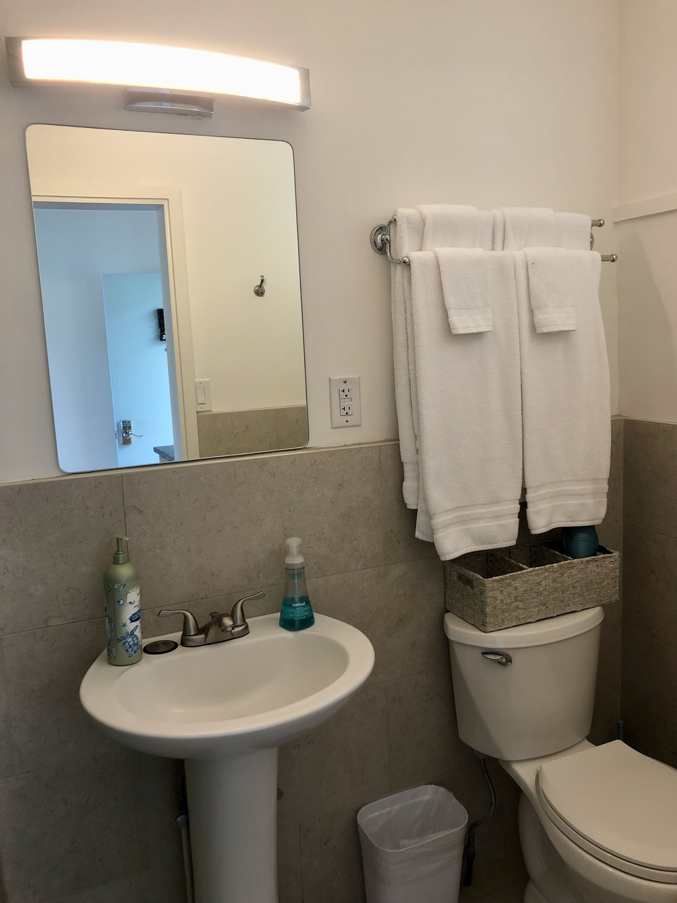 Baño con lavamanos, espejo y dos toallas colgadas en un perchero.