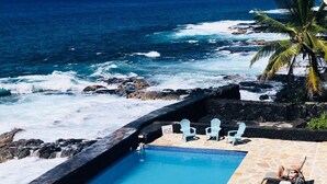 Piscina con vistas al océano, sillas blancas y un cartel que indica la presencia de socorristas.