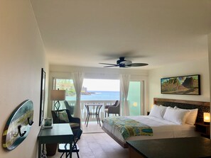 Une chambre d’hôtel équipée d’un lit, d’un bureau, d’une chaise, d’un balcon avec vue sur l’océan et d’un ventilateur de plafond.