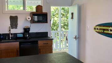Una cocina con armarios de madera, encimera negra, lavavajillas integrado, microondas y ventana con vistas a follaje.