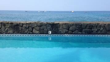 A swimming pool with a stone wall and a view of the sea.