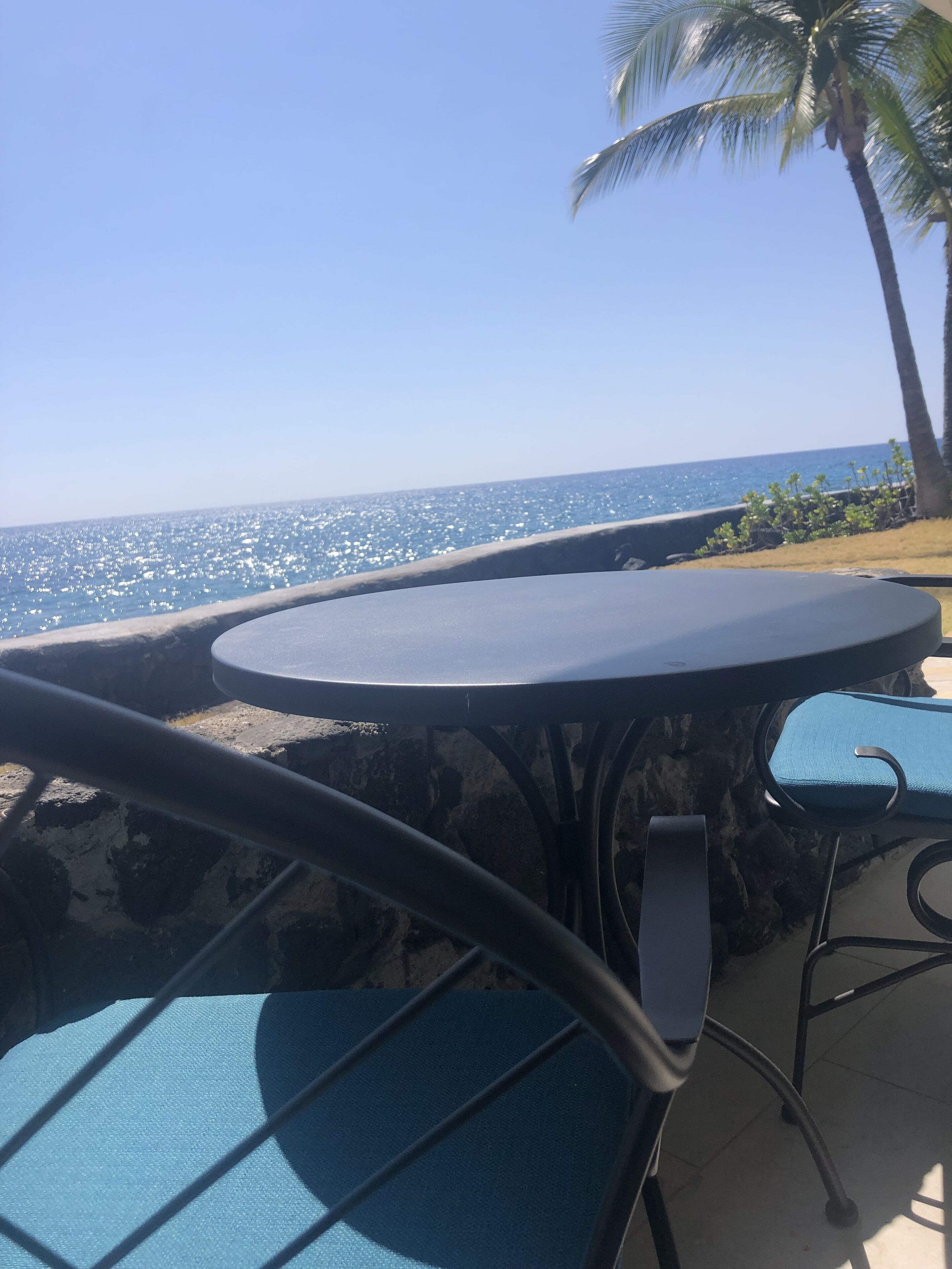 A seaside patio with a table and chairs, overlooking the ocean.