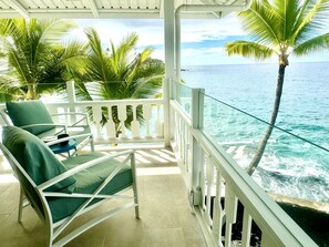 Un balcon avec des balustrades blanches, deux fauteuils verts avec des coussins et une vue sur l’océan.