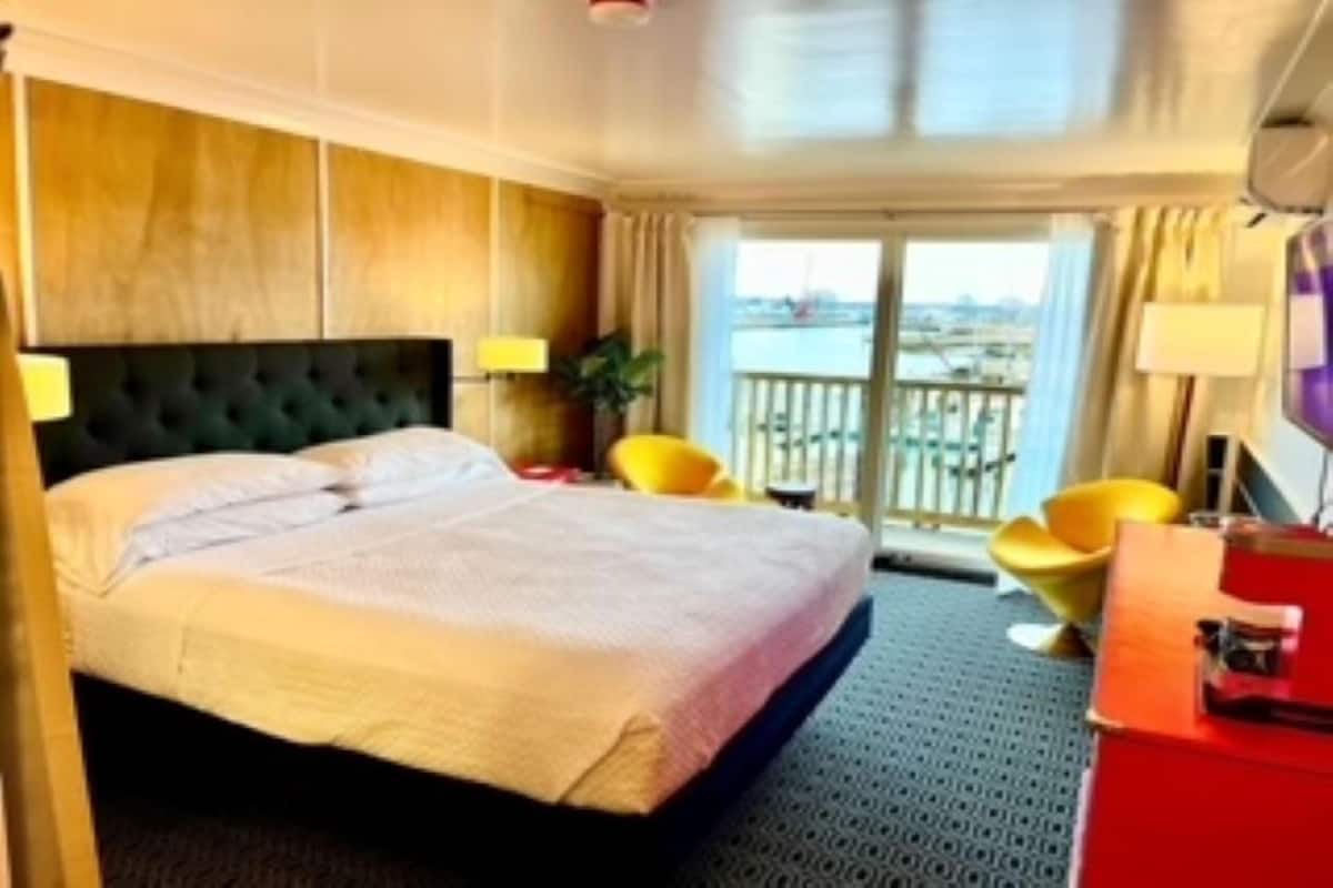 A hotel room with a large bed, a desk, a chair, and a balcony with a view.
