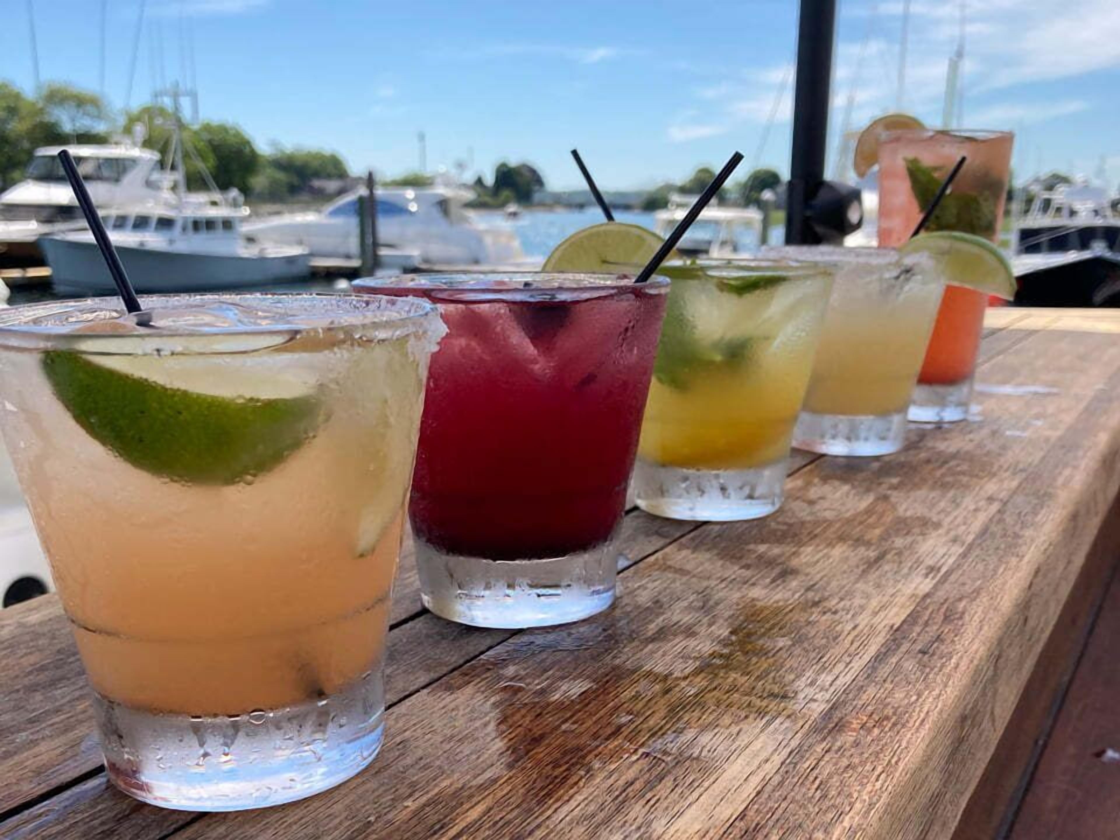 A wooden table with four glasses of iced drinks, each with a lime wedge and a straw.