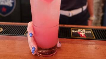 Un bar con una bebida en un vaso alto, una persona al fondo y un logotipo en la barra.