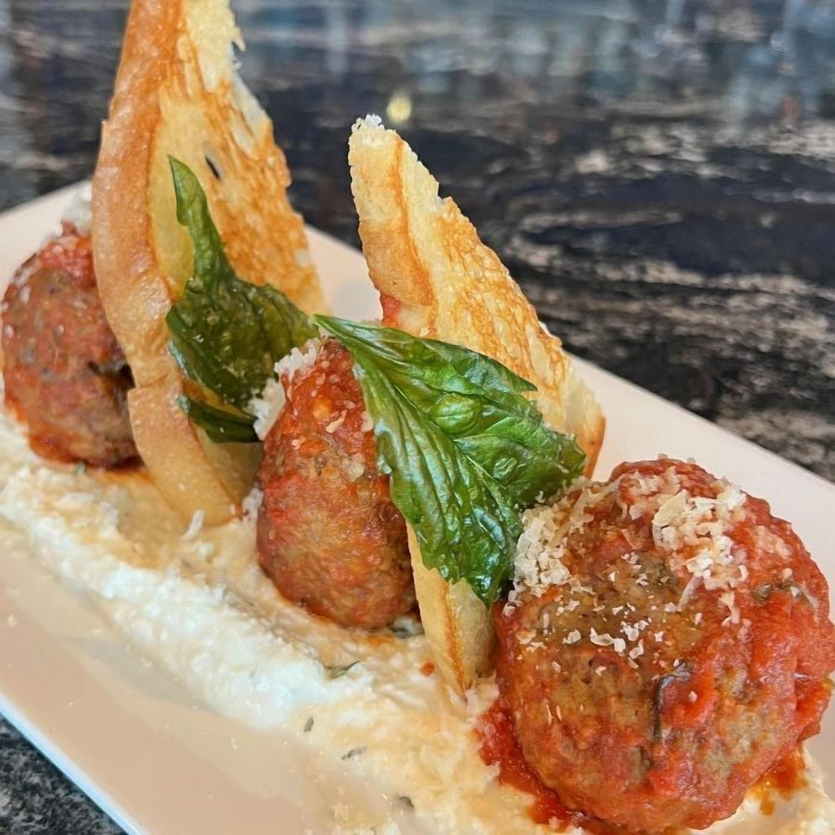 A plate of meatballs with a creamy sauce and a garnish of basil leaves.