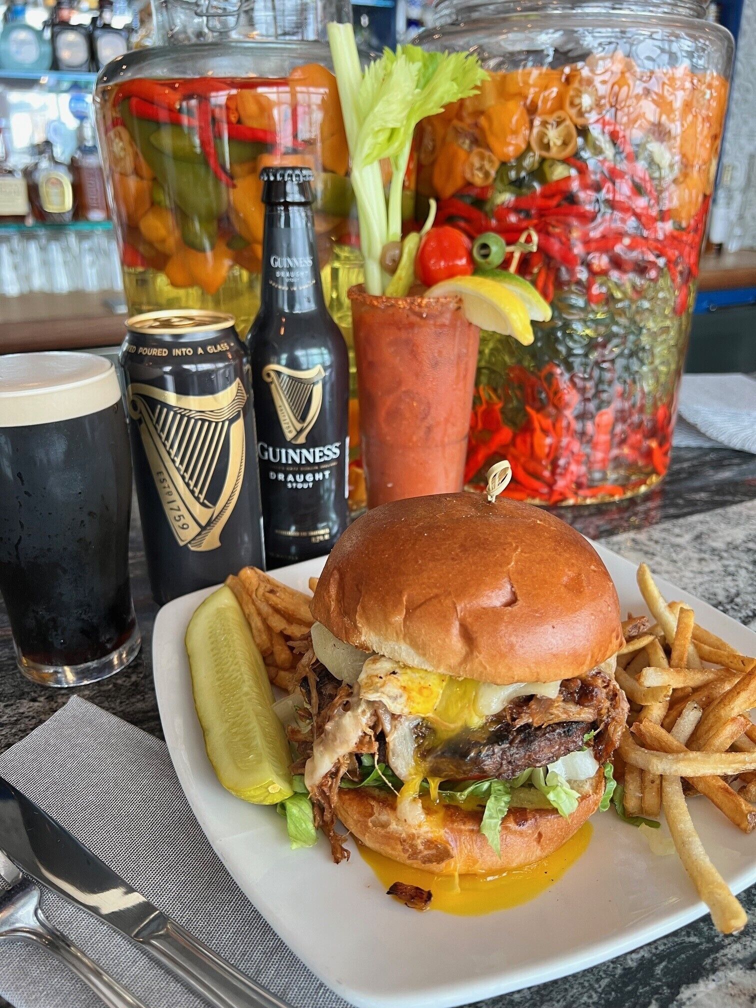 Una comida con un sándwich, papas fritas y una bebida, junto con un tarro grande de pepinillos y dos botellas de cerveza Guinness.