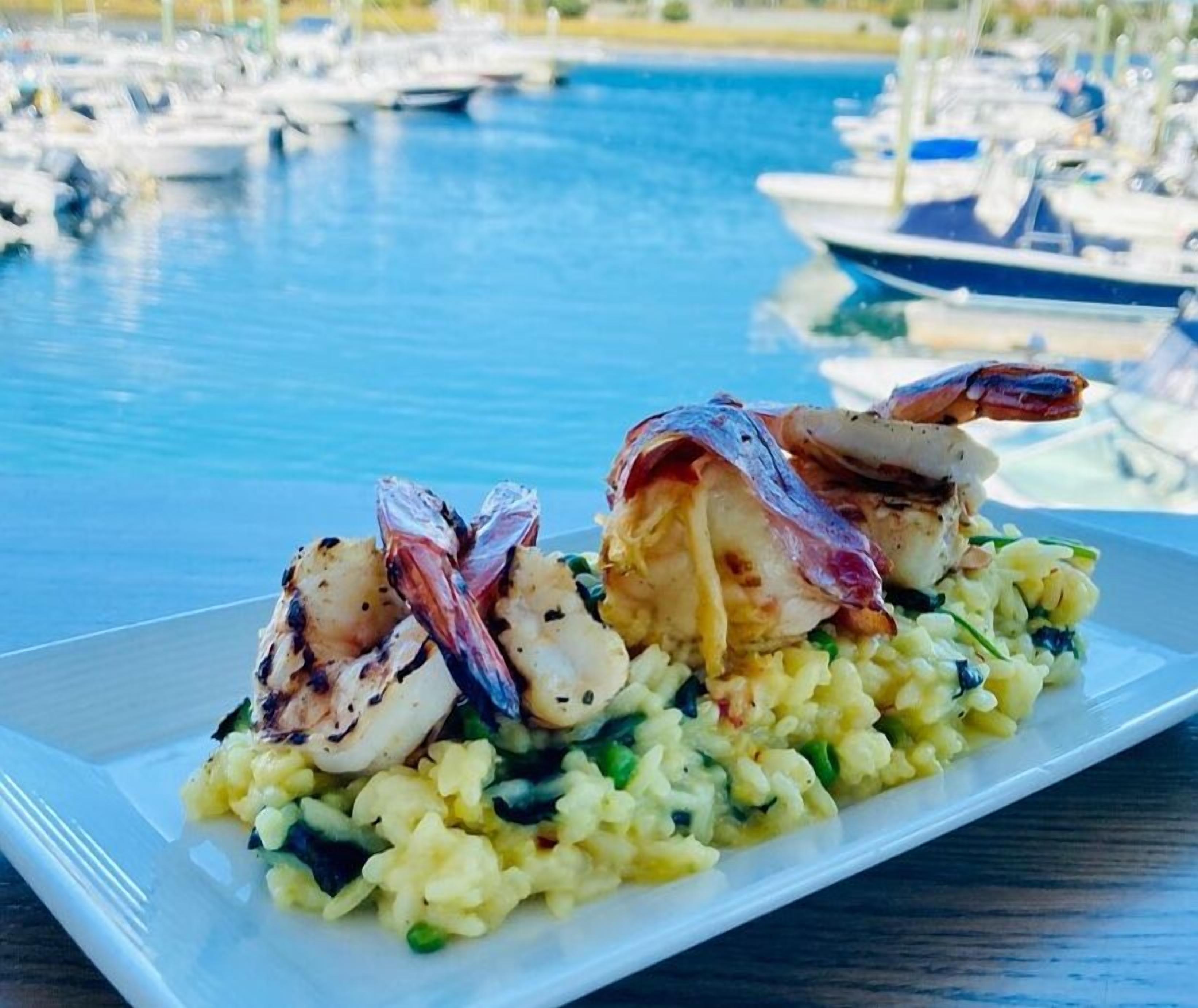 Un plato de mariscos con camarones a la parrilla y vieiras sobre risotto, servido en un plato blanco.