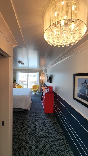 Ett hotellrum med en säng, ett skrivbord, en stol, en tv och en kristallkrona.