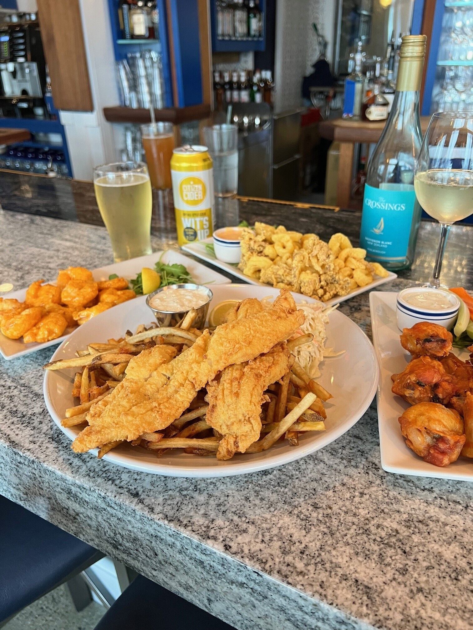 A bar counter with various dishes including fried fish, fries, and seafood, along with drinks and condiments.