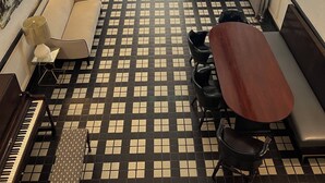 A room with a checkered floor, a piano, a sofa, a table, and a bench. - Nash Hotel (Berkeley)