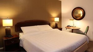 A hotel room with a large bed, two bedside tables with lamps, a round mirror on the wall, and a chair. - Nash Hotel (Berkeley)