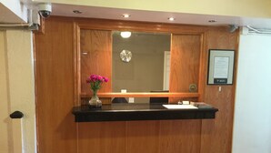 A wooden reception desk with a black countertop, a vase with pink flowers, a clock, and a framed sign indicating WIFI availability. - Nash Hotel (Berkeley)