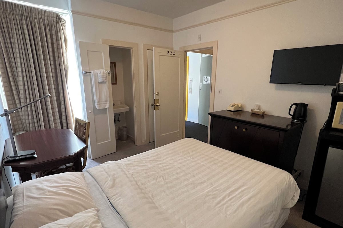 A hotel room with a large bed, a desk, a television, and a bathroom visible through an open door.