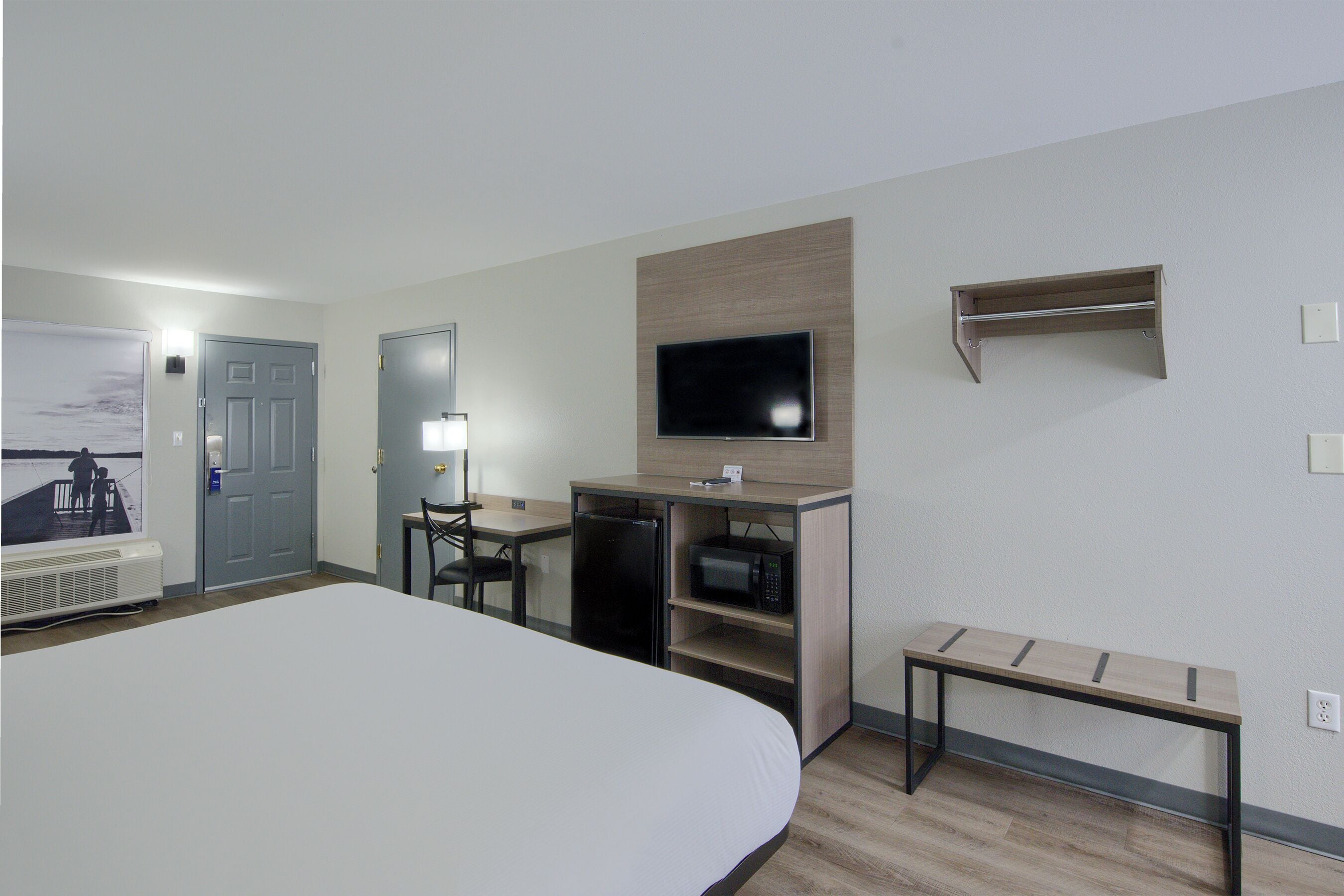 A hotel room with a large bed, a desk with a computer, a microwave, and a television on the wall.