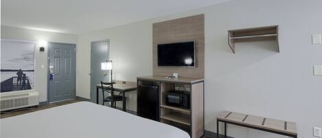 Ein Hotelzimmer mit einem großen Bett, einem Schreibtisch mit Computer, einer Mikrowelle und einem an der Wand befestigten Fernseher.