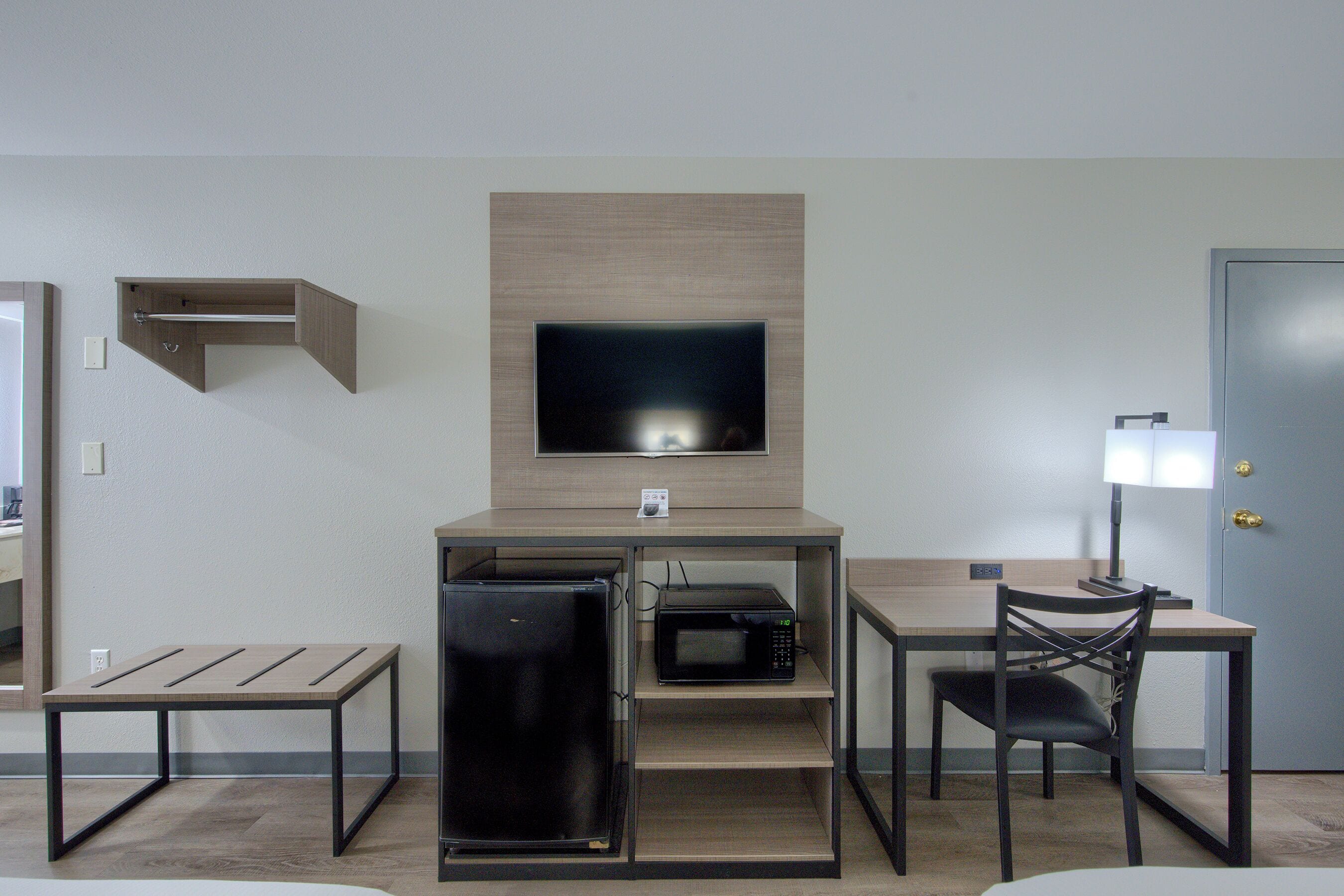 Et lille hotelværelse med tekøkken, et fladskærms-tv, et skrivebord med stol og en dør.