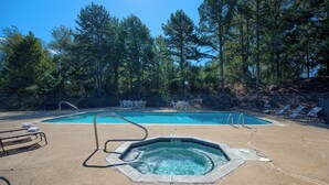 A swimming pool with a hot tub, lounge chairs, and a fenced area with trees in the background. - Hotsprings Village Inn (Hot Springs Village)