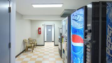 A hallway with a checkered floor, vending machines, and plastic chairs.