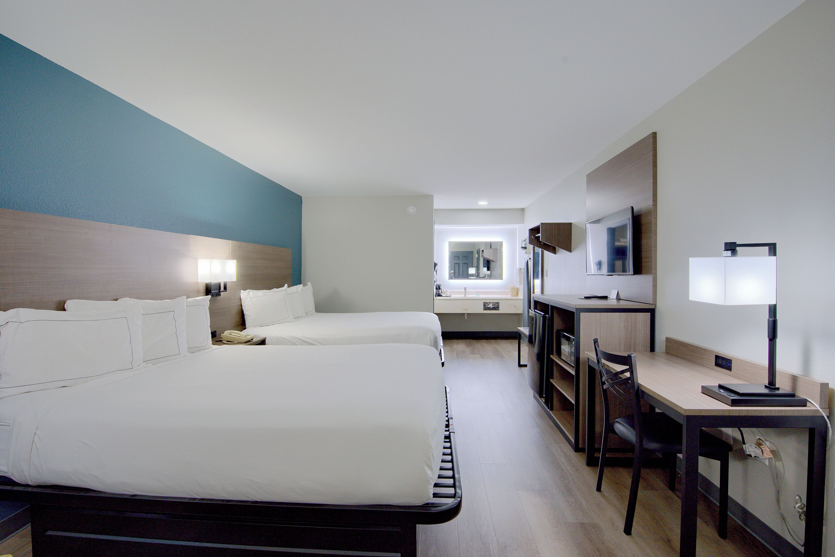 Une chambre d’hôtel avec deux lits, un bureau, une chaise, une télévision et une fenêtre.