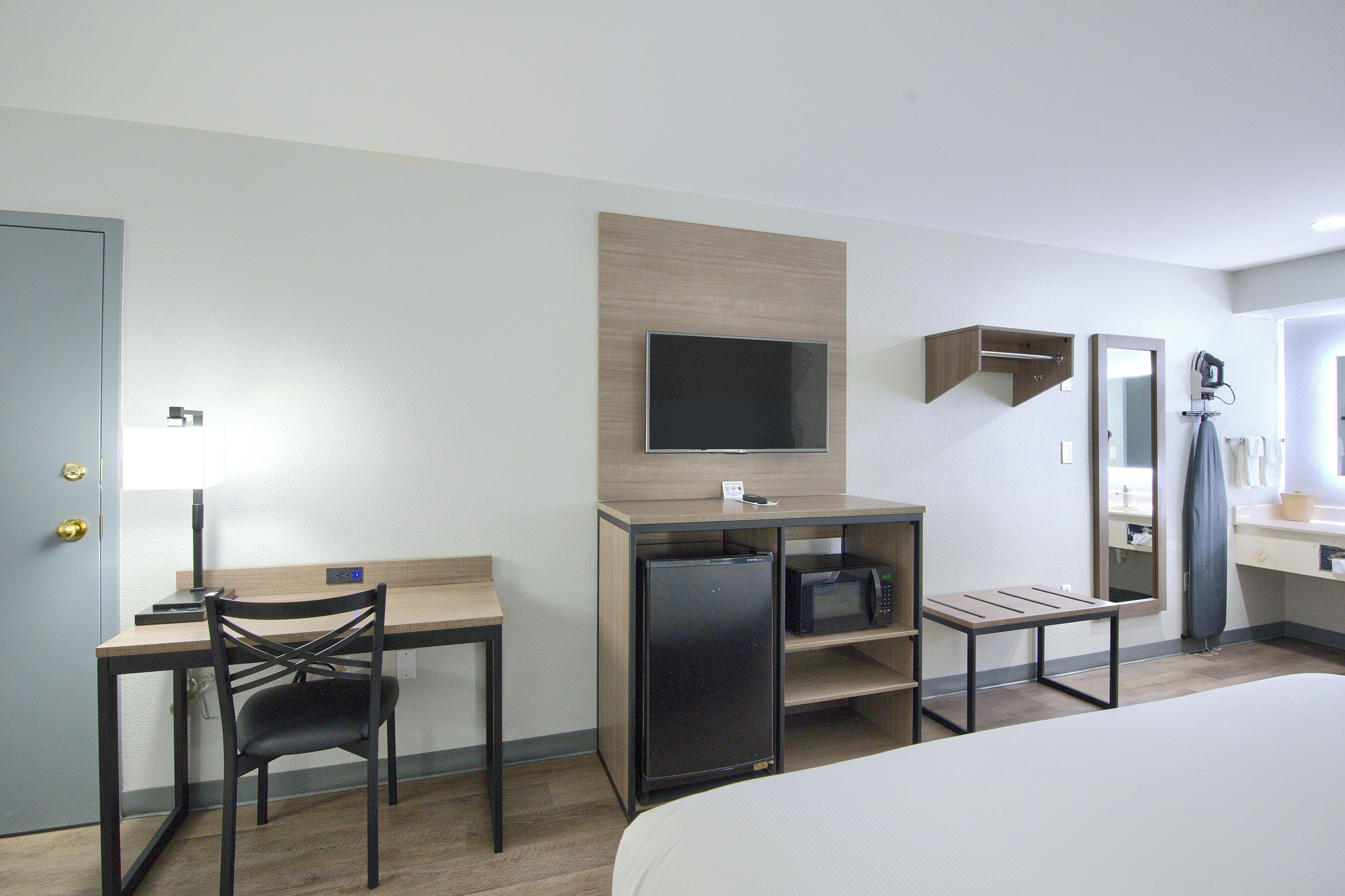 Una habitación de hotel con cama, escritorio con silla, televisión, microondas y una mesita.