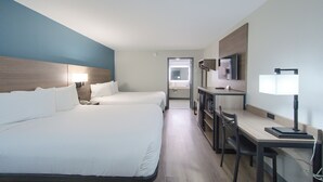 A hotel room with two beds, a desk, a chair, a TV, and a bathroom visible through an open door. - Hotsprings Village Inn (Hot Springs Village)