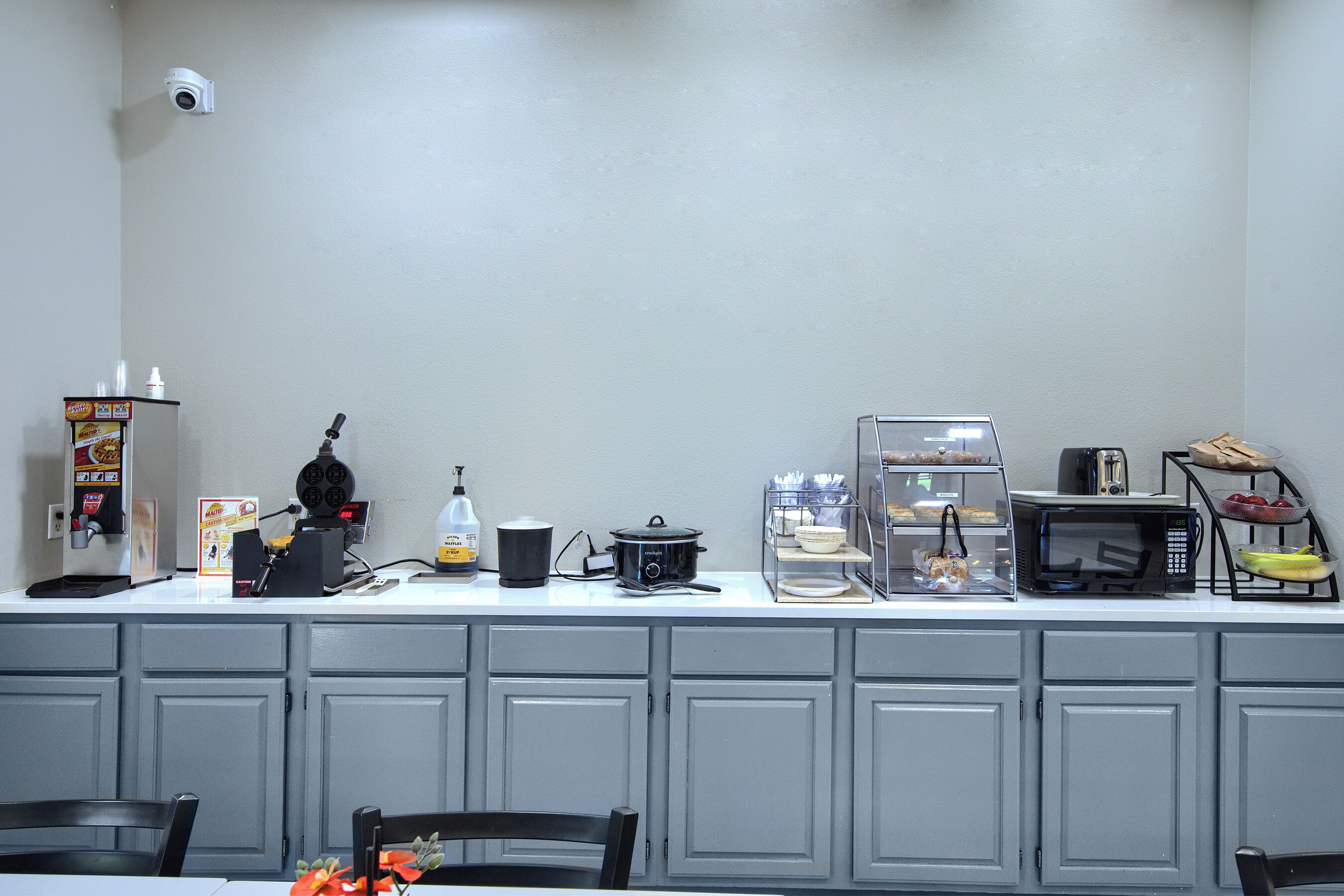 Zona de cuina amb cafetera, microones, torradora i vitrina amb productes alimentaris.