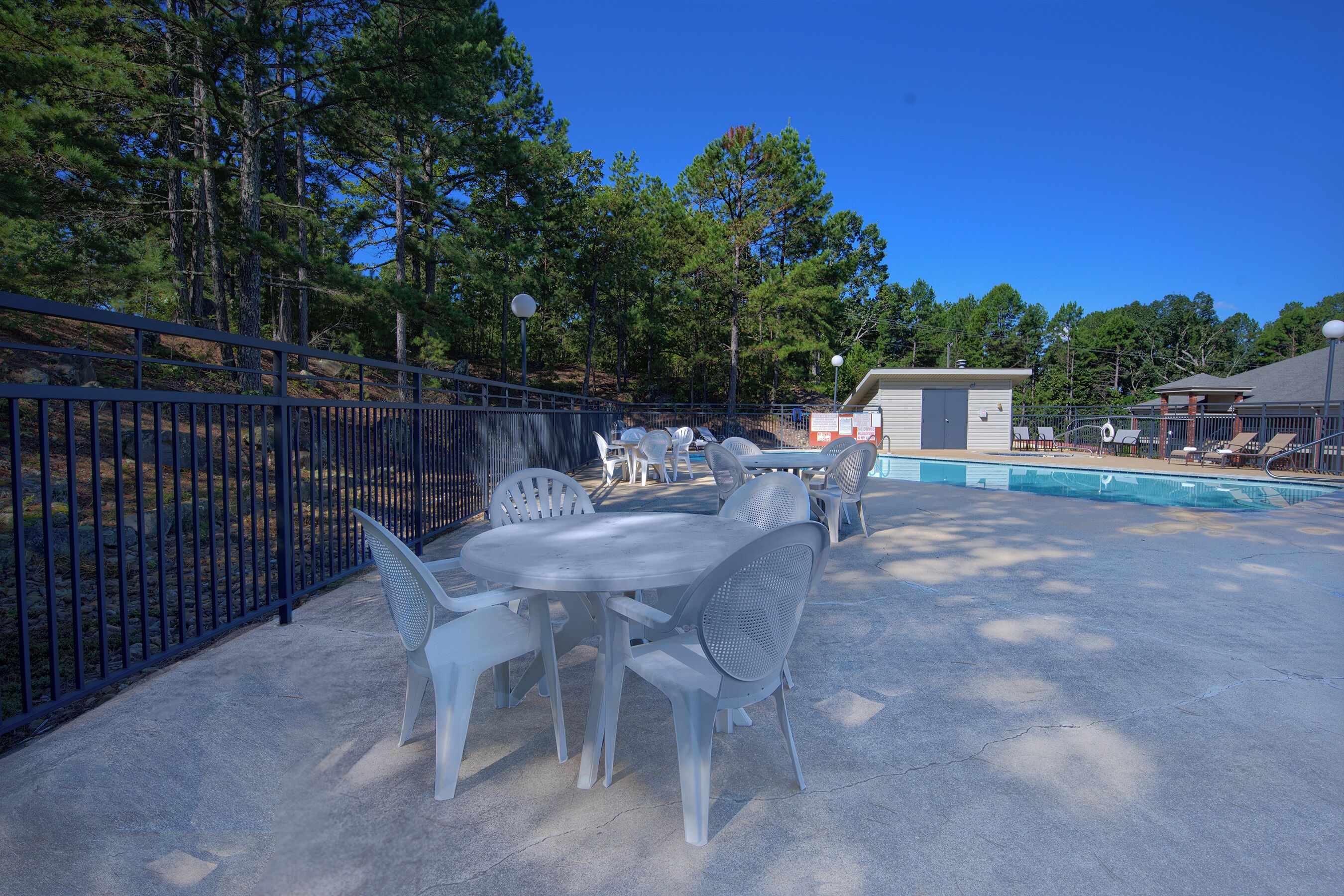 Un espace extérieur aménagé en patio, avec une piscine, entouré d’une clôture, et comprenant une table et des chaises.