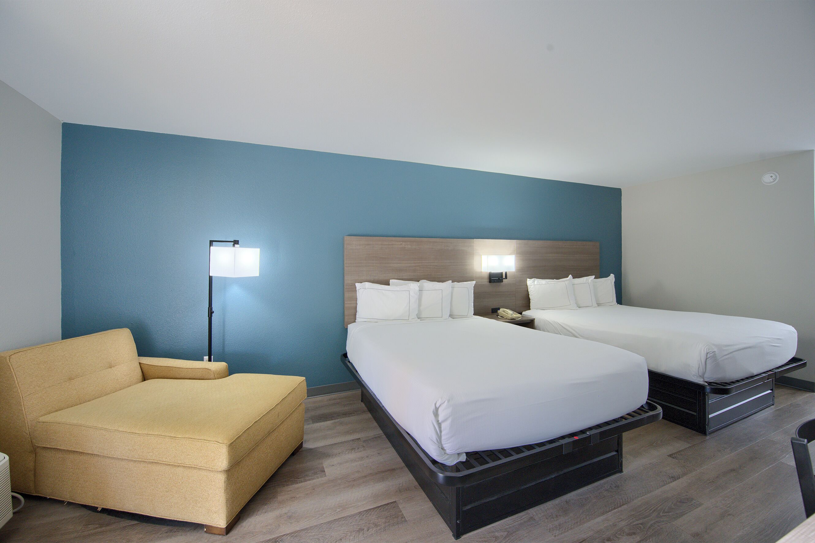 A hotel room with two beds, a sofa, a lamp, and a nightstand.
