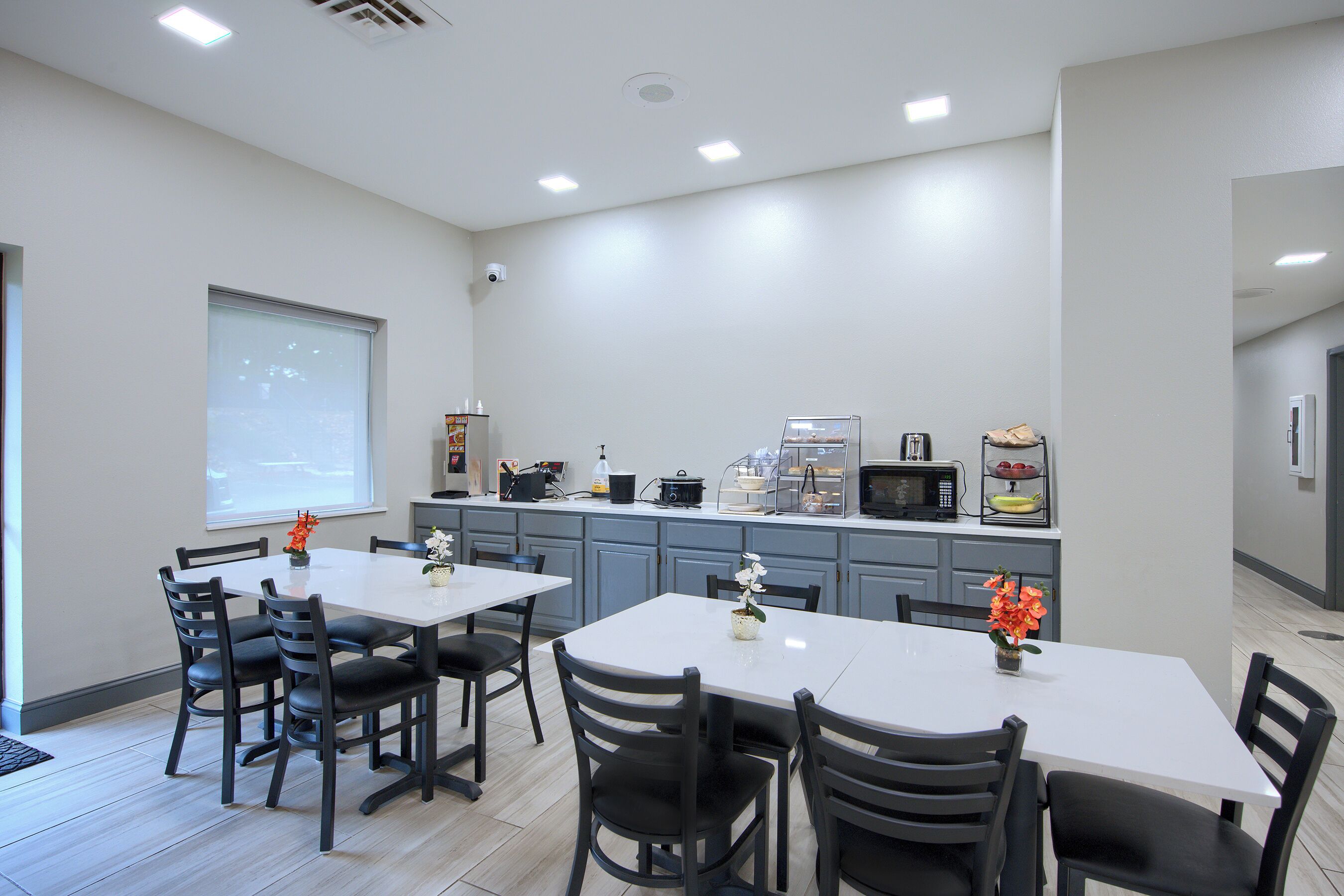 A modern kitchen with a white countertop, grey cabinets, and a dining area with a white table and black chairs.
