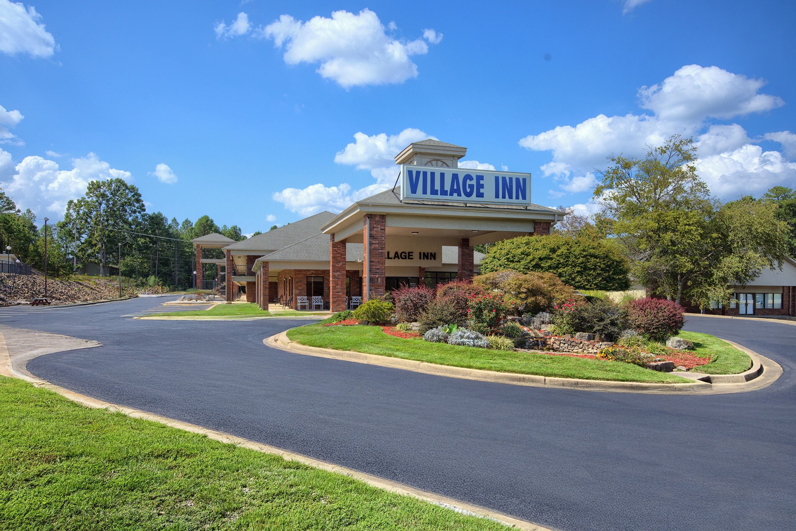A Village Inn hotel with a curved driveway, landscaped garden, and a clear blue sky.