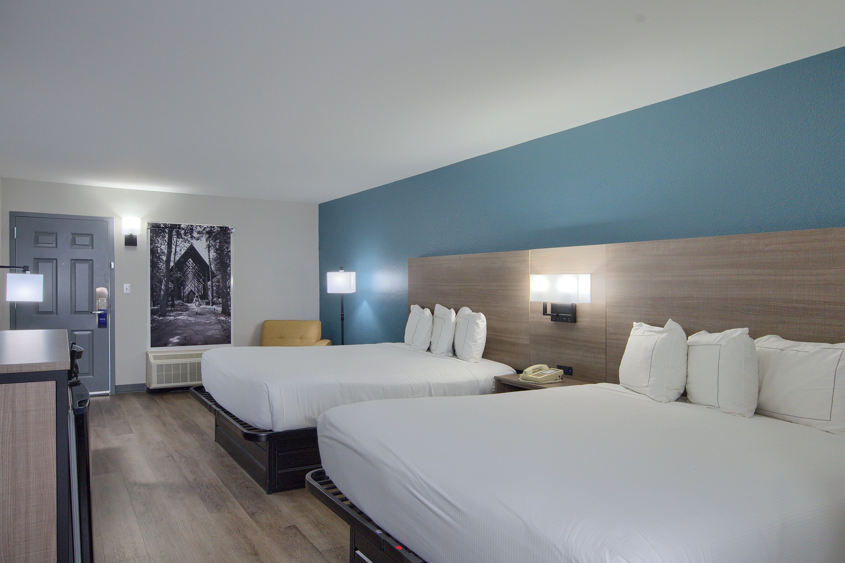 A hotel room with two beds, a desk, a chair, a telephone, and a wall-mounted lamp.