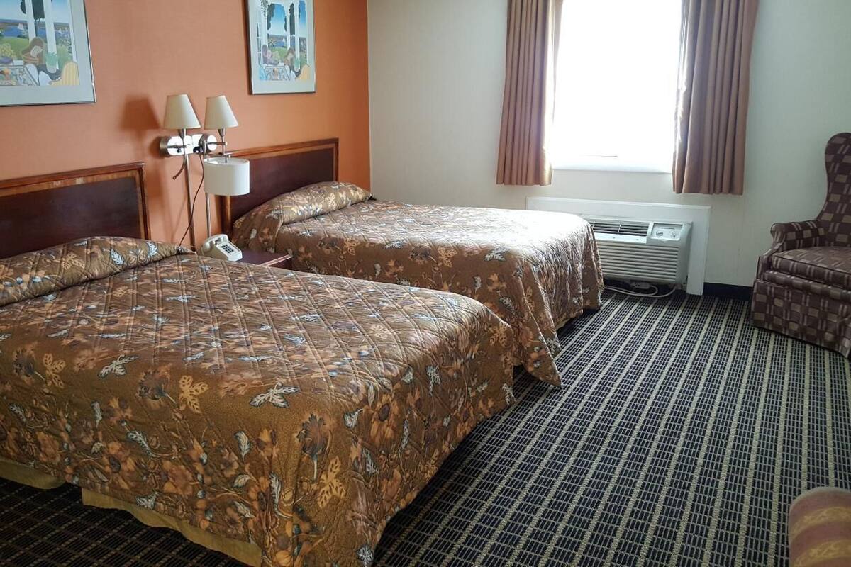A hotel room with two beds, a chair, a phone, and artwork on the walls.