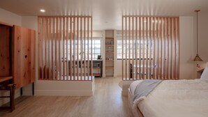 A modern bedroom with a wooden wardrobe, a bed with a white duvet, and a view of a kitchen and dining area through a wooden partition. - Best Friends Roadhouse and Mercantile (Kanab)