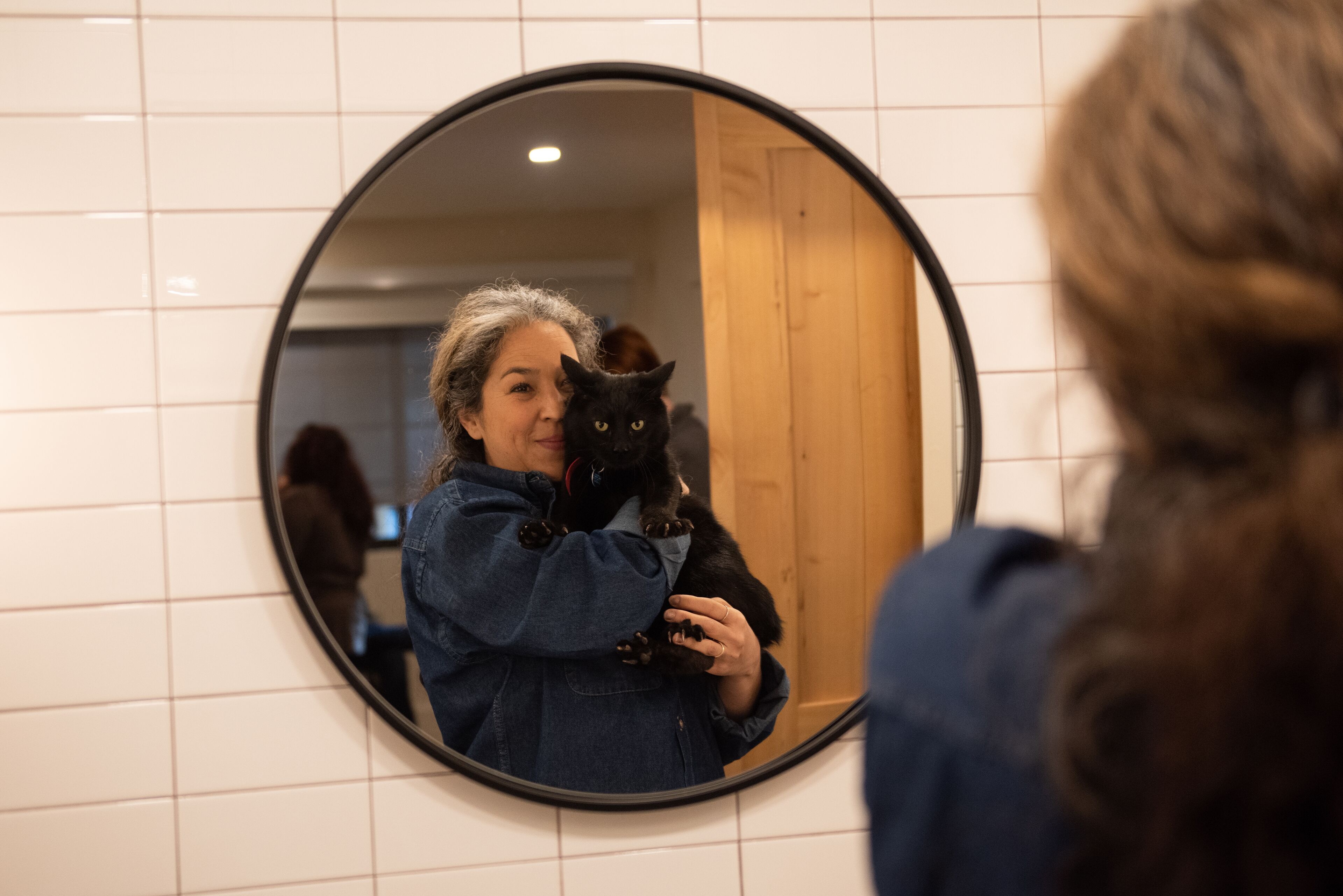 Une personne tenant un chat devant un miroir rond.
