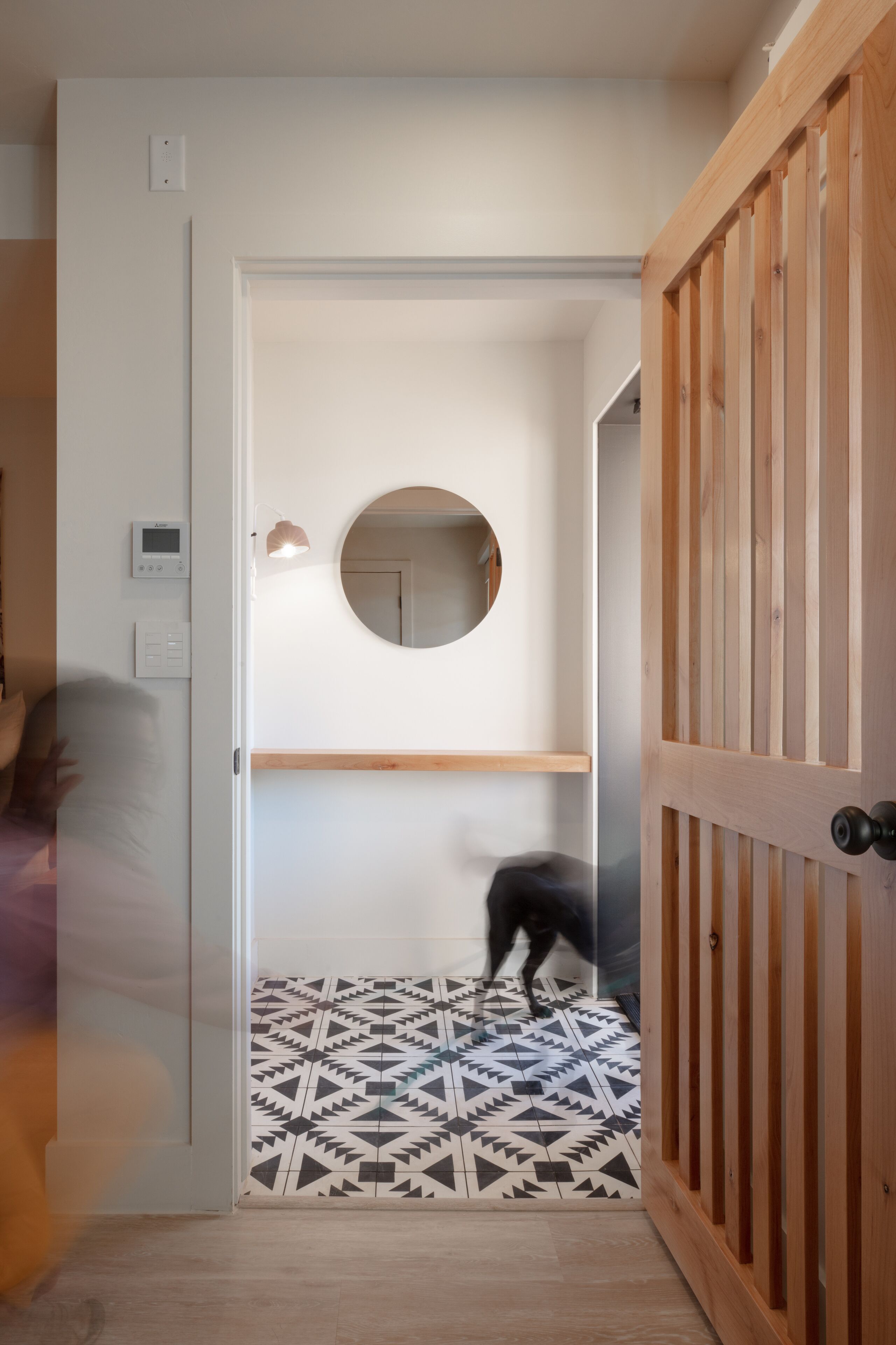 A hallway with a patterned floor, a round mirror on the wall, and a wooden door.