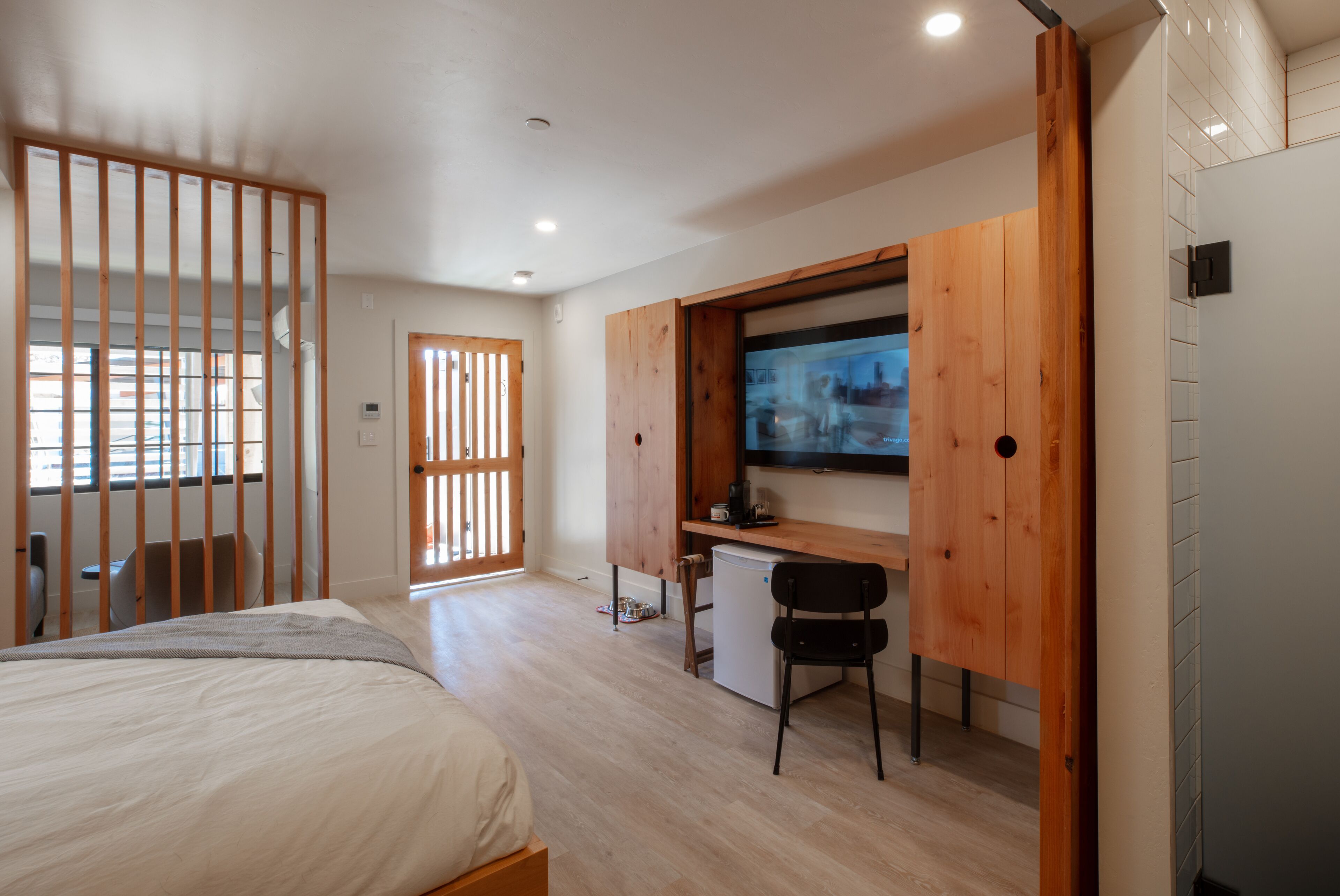 A bedroom with a bed, a desk with a chair, a television, and a wooden partition.