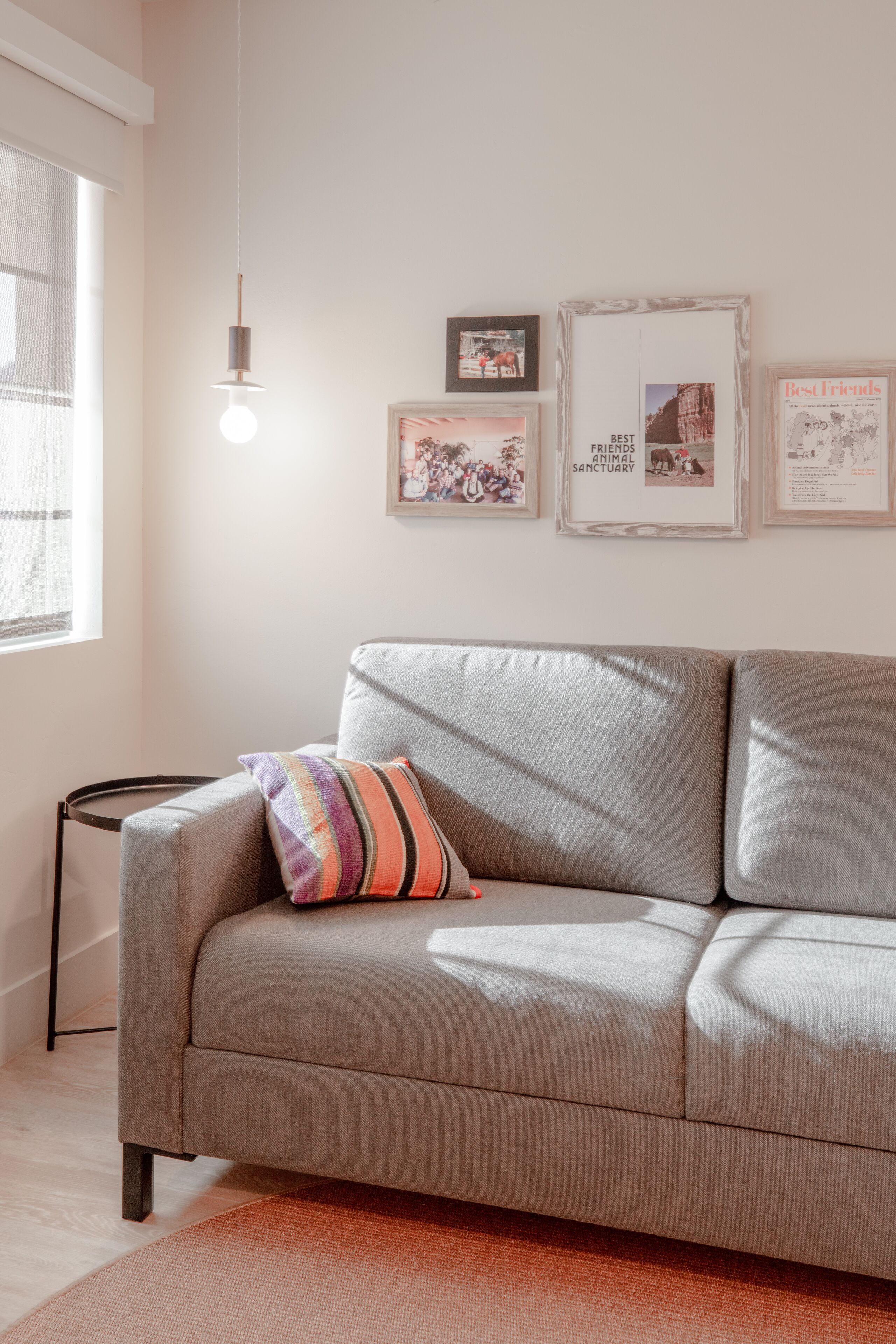 A modern living room with a grey sofa, a colorful striped pillow, and framed pictures on the wall.