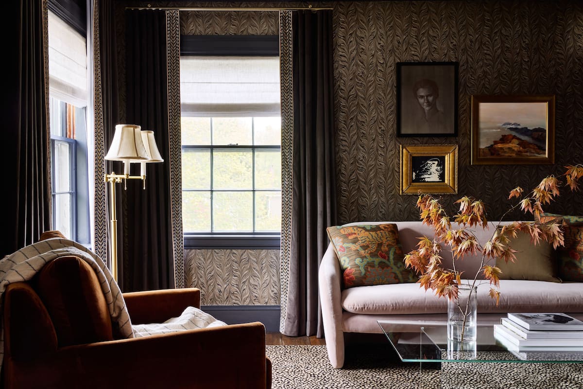 A living room with a sofa, armchair, and a coffee table with books and a vase of dried flowers.